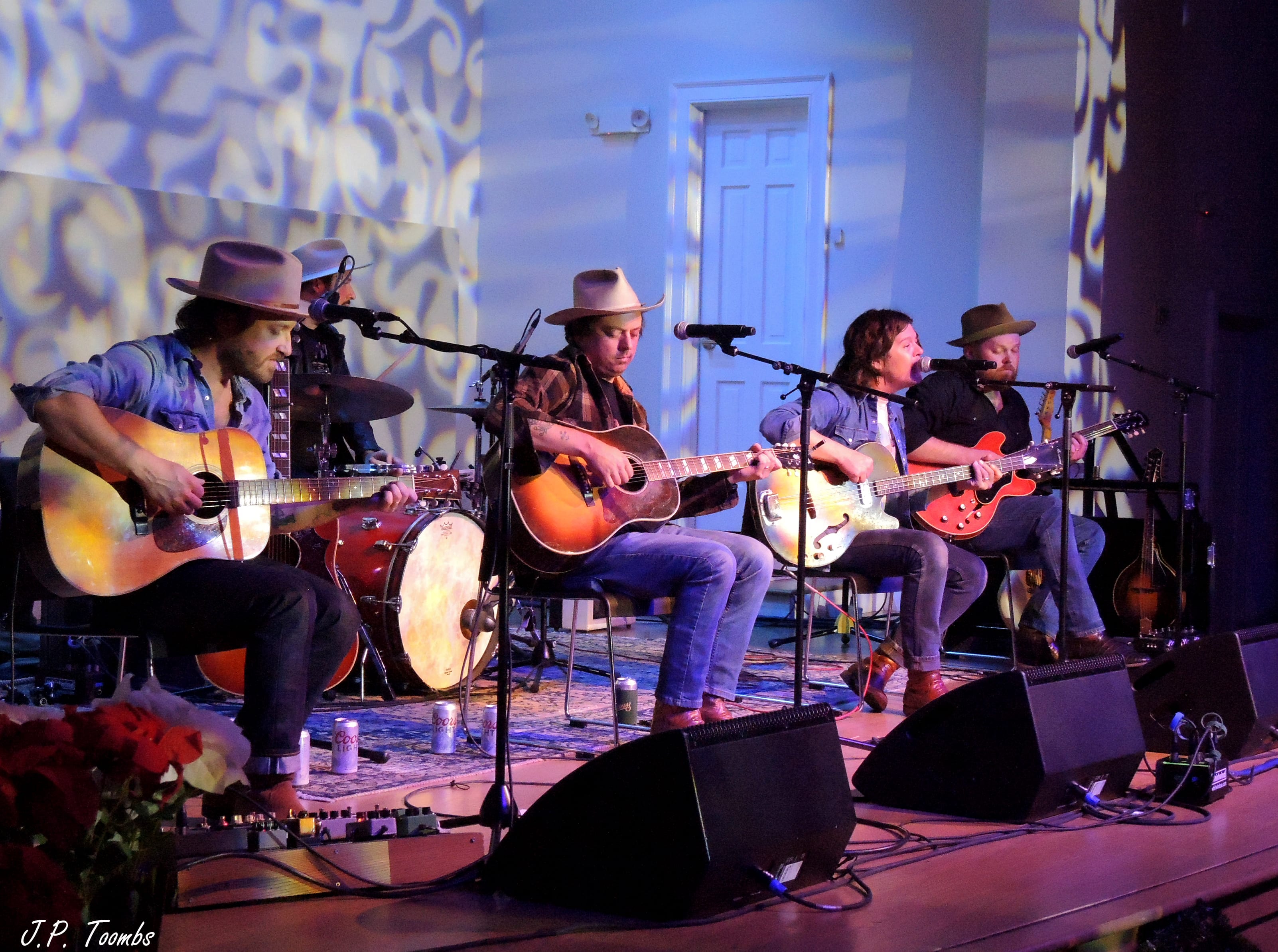 The Wild Feathers sit in a row with acoustic instruments during the tenth-anniversary performance at Riverside Revival.