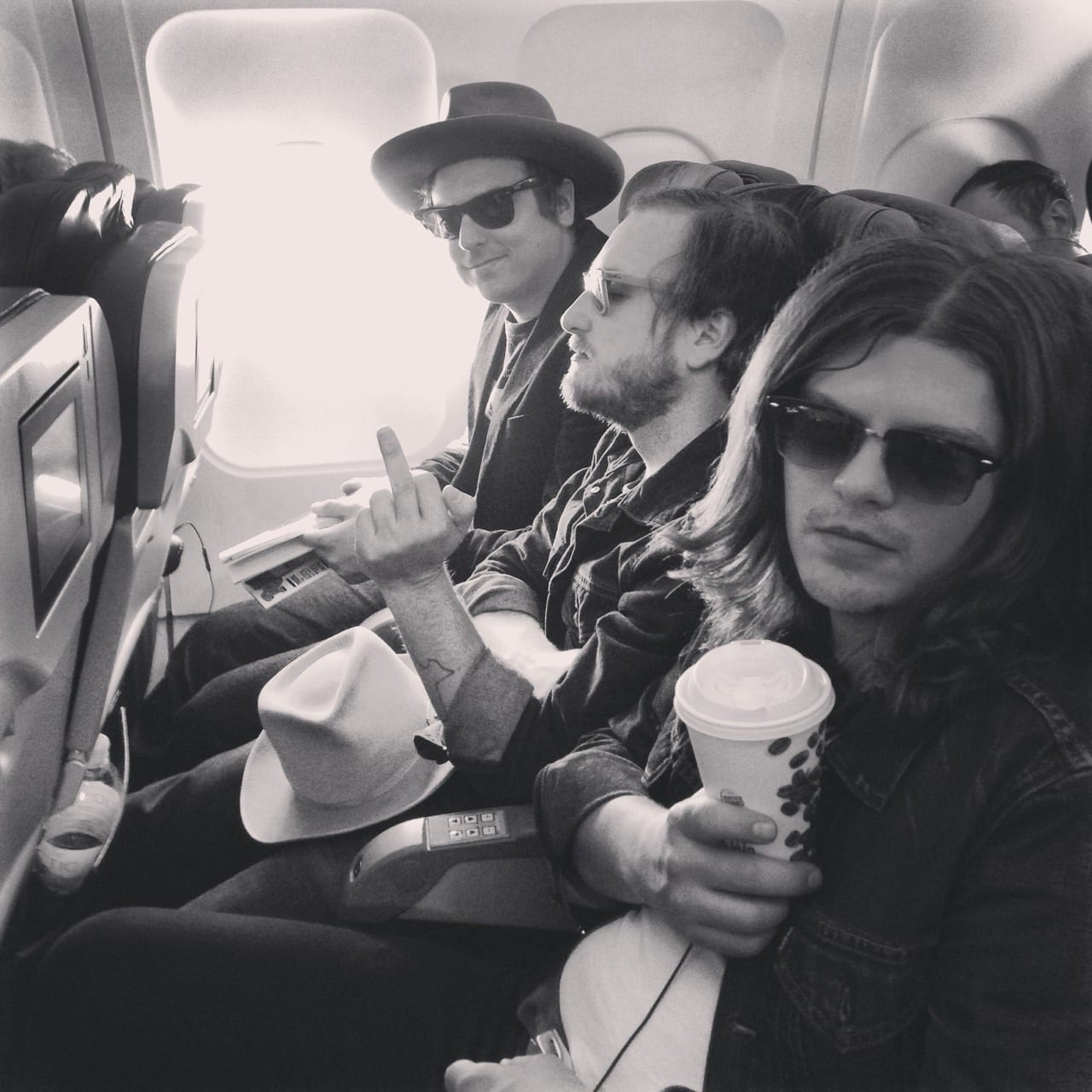Black-and-white photograph of three unidentified Wild Feathers members seated together on an airplane.
