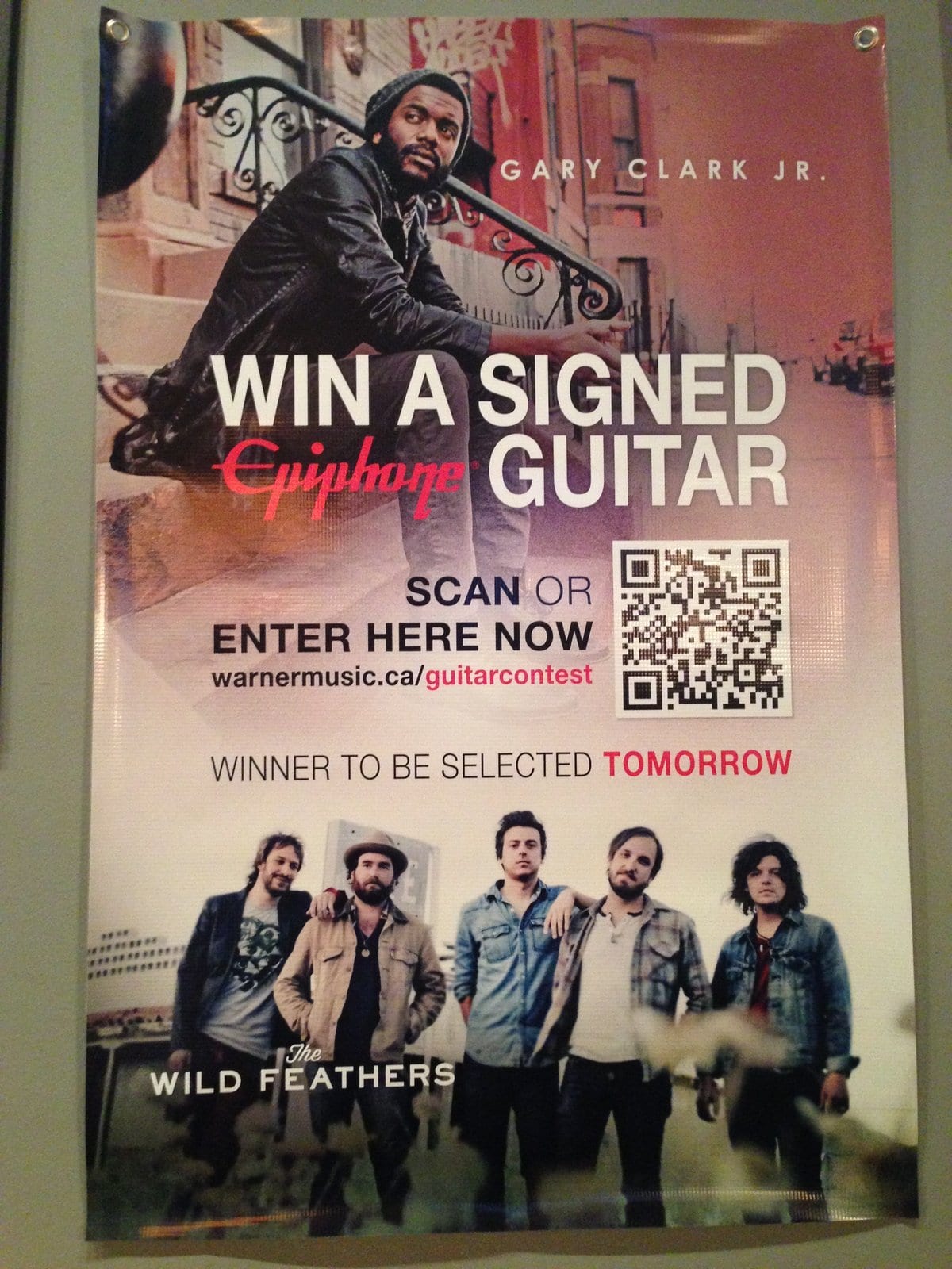 A promotional display for a Gary Clark Jr. guitar giveaway above an image of The Wild Feathers.