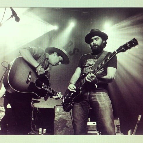 Two unidentified Wild Feathers guitarists playing together onstage in a monochrome photograph.