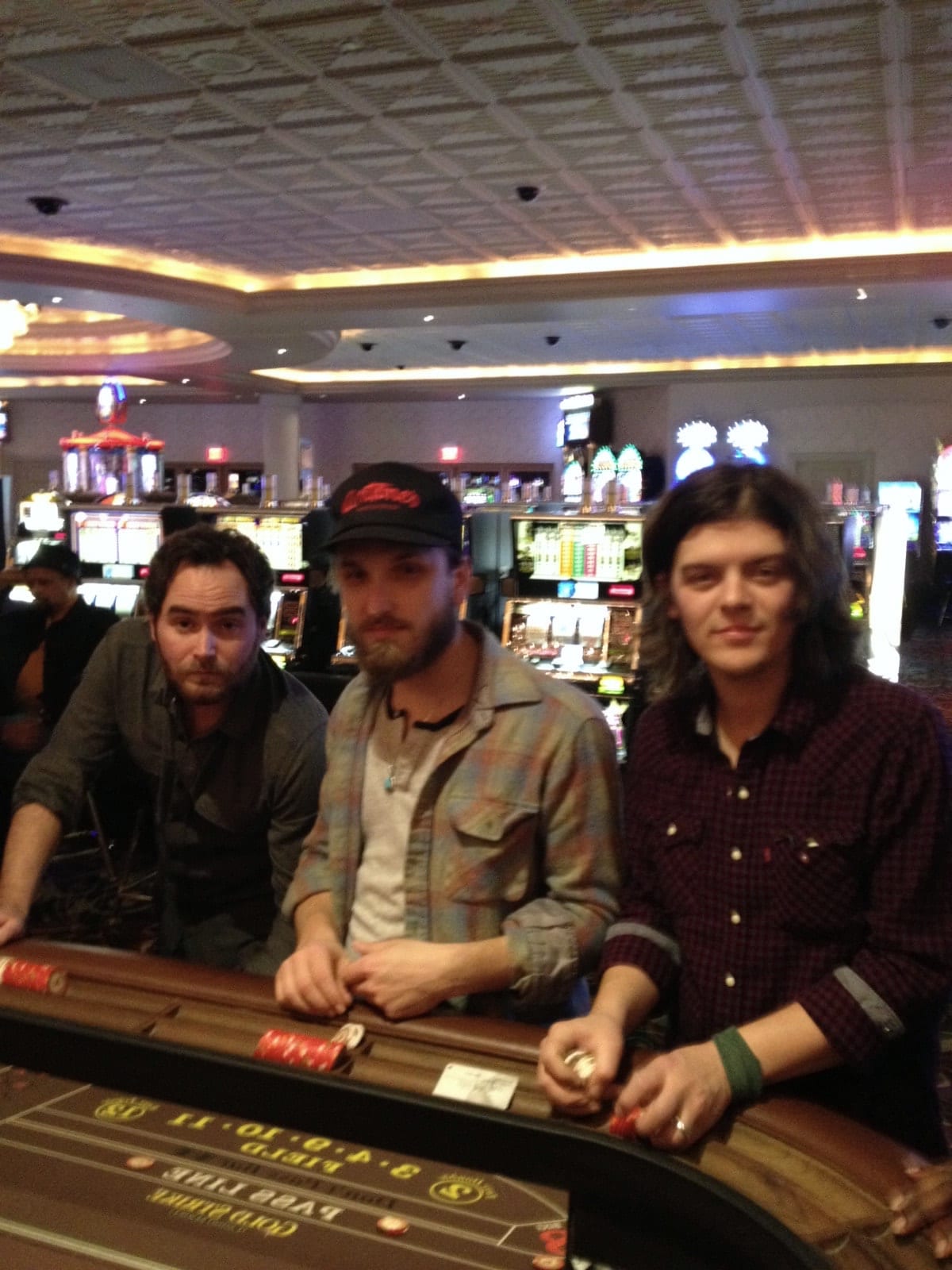 Three members of The Wild Feathers seated together at a casino gaming table.