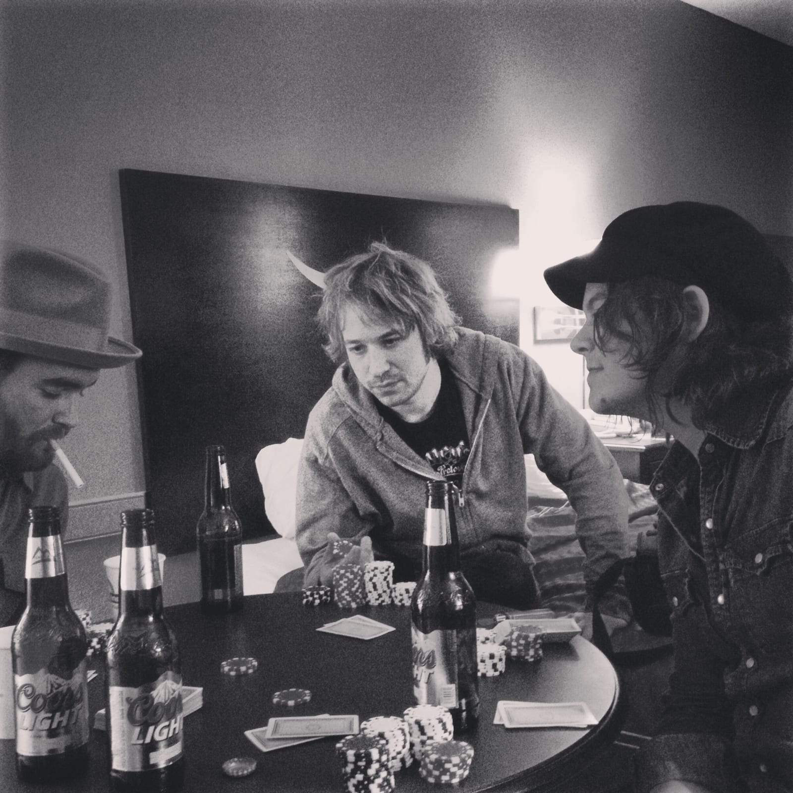 Members of The Wild Feathers gathered around a hotel-room poker table in a black-and-white square photograph.