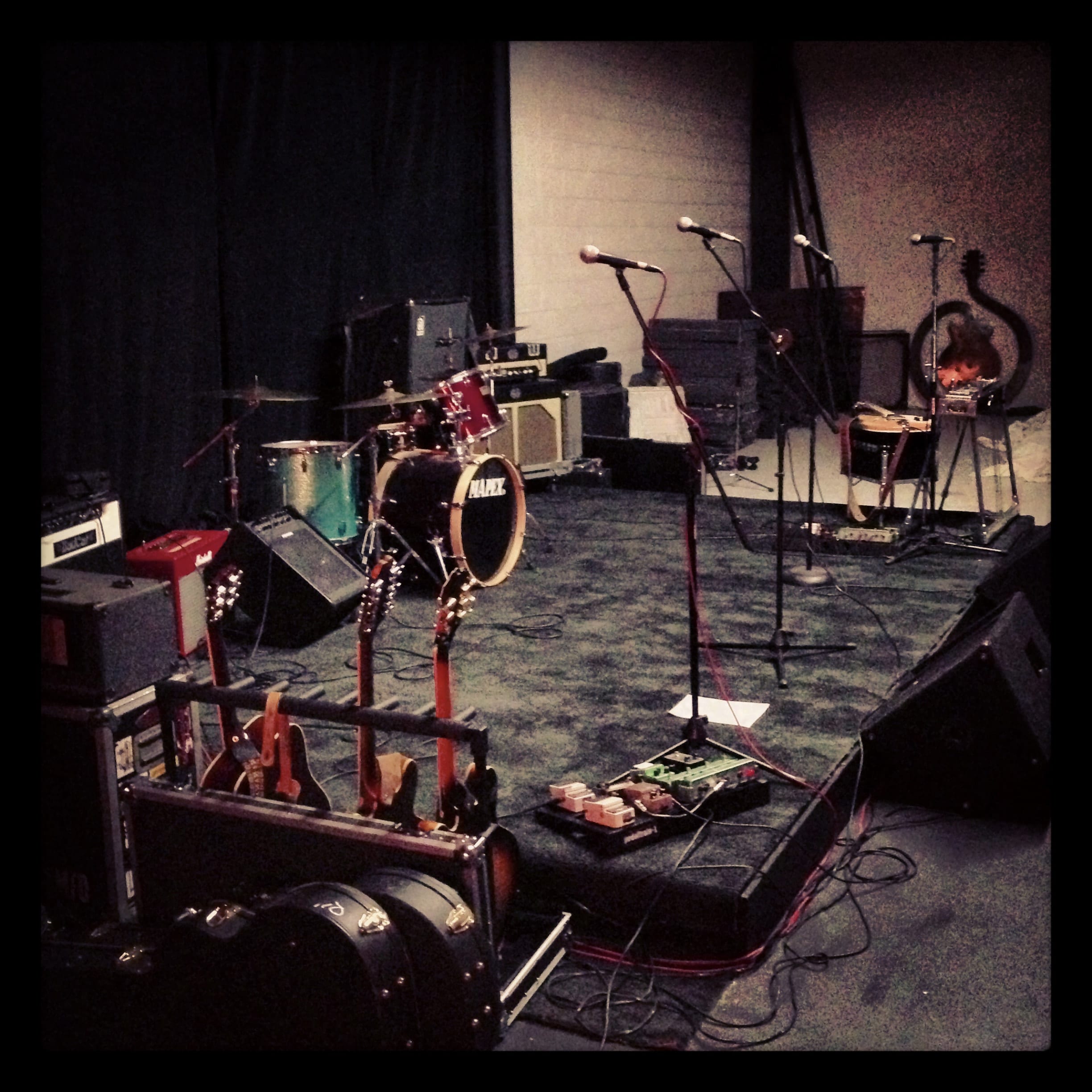 An empty prepared concert stage with drums, amplifiers, microphones, and floor monitors.